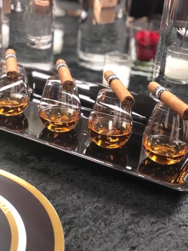 Glasses of whiskey each topped with a cigar on a silver tray