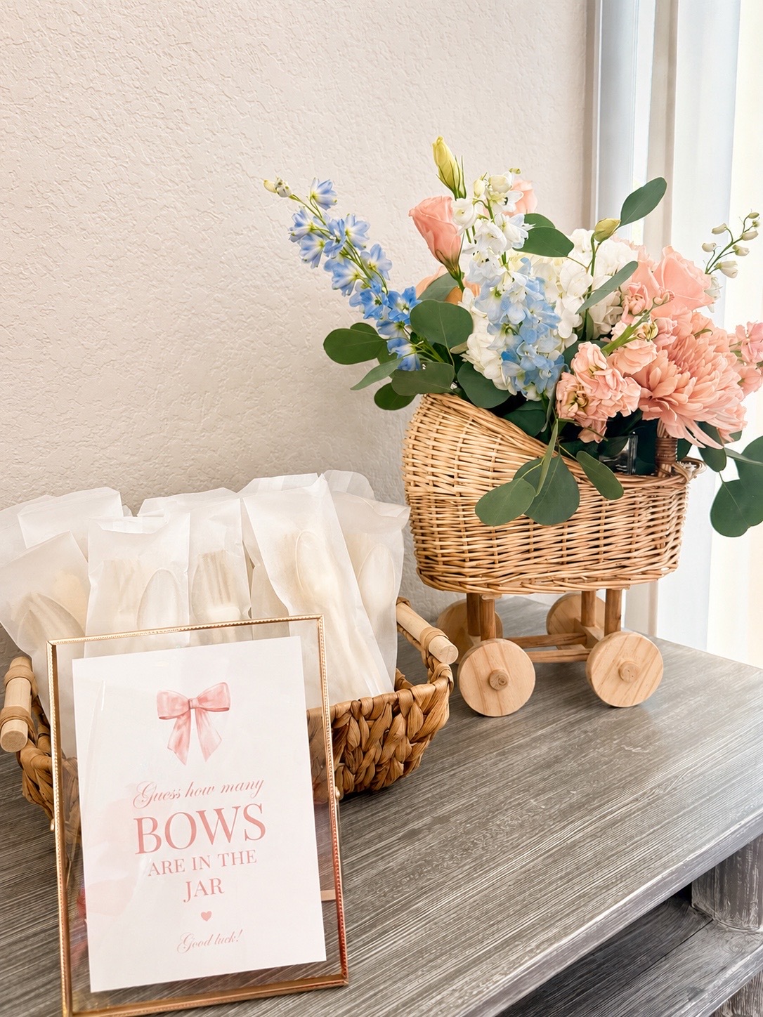 A baby shower game sign beside a wicker flower cart filled with peach, cream, and blue blooms at Magnolia Studio