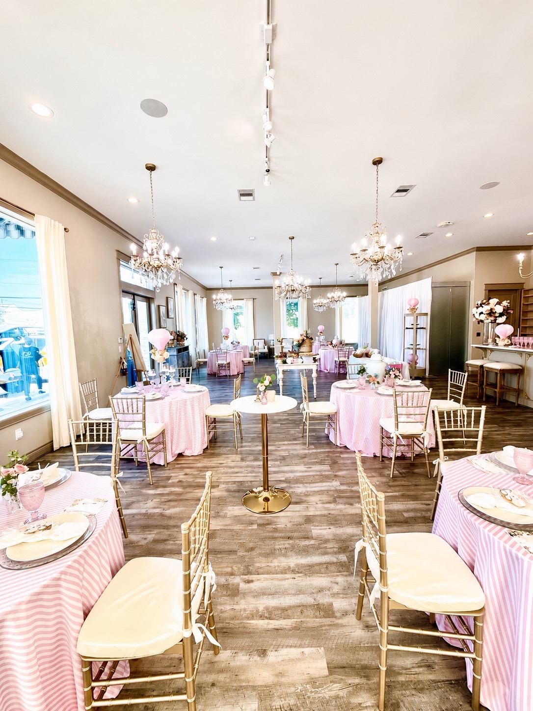 The Magnolia Studio styled for a Parisian-themed baby shower with pink striped tables, champagne gold chairs, and crystal chandeliers