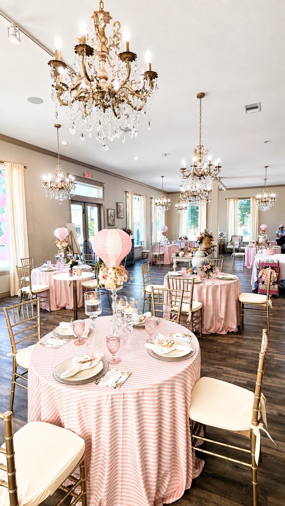 The Magnolia Studio event room styled in pink striped linens with champagne gold chairs beneath crystal chandeliers for a Parisian-themed baby shower