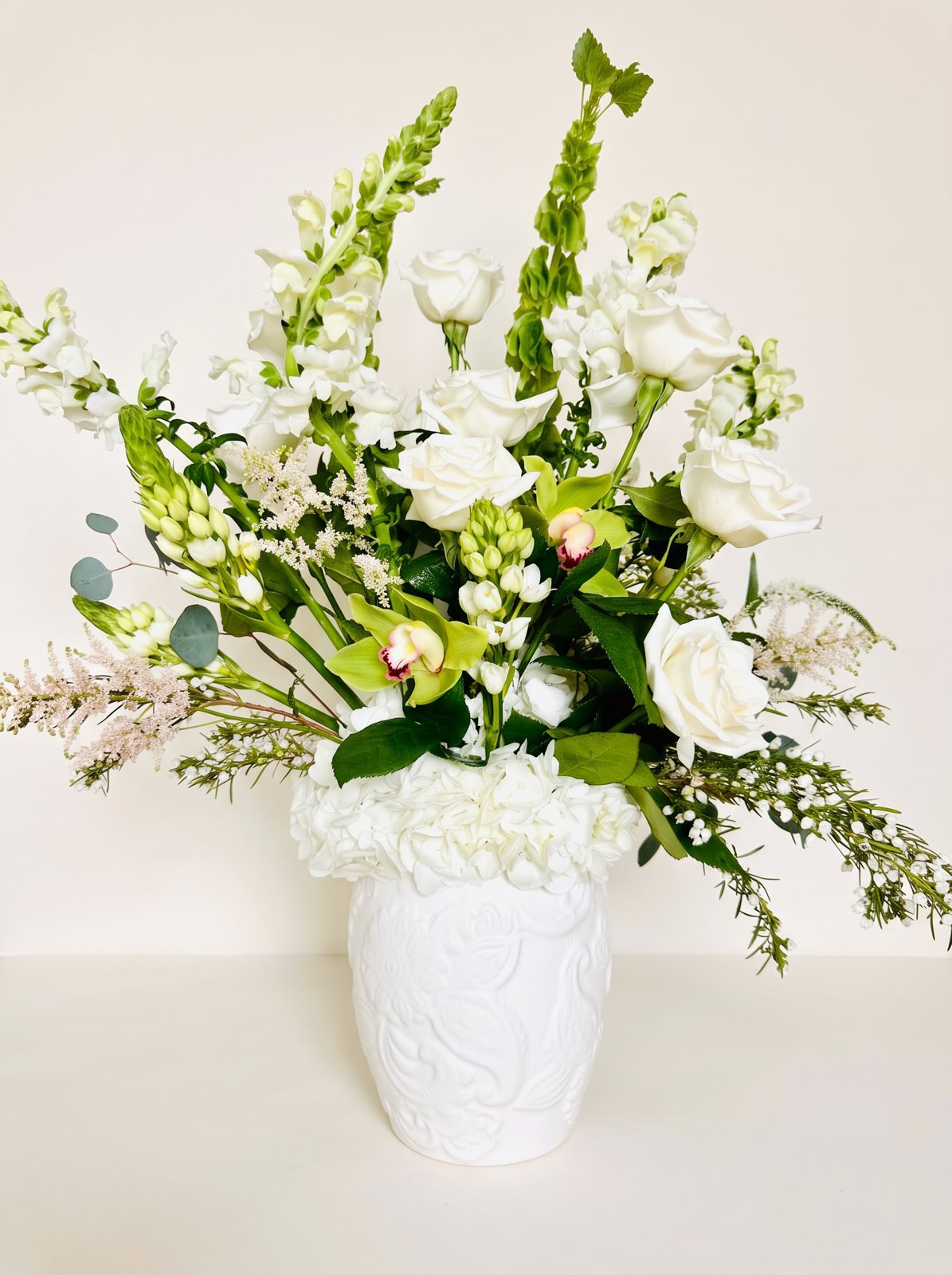 White roses, snapdragons and green orchids in an embossed white vase